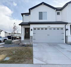 View of front of property with stone siding, a shingled roof, driveway, and a garage