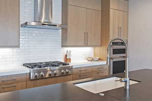 Kitchen featuring wall chimney exhaust hood, stainless steel appliances, modern cabinets, and decorative backsplash