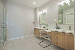 Bathroom featuring a shower stall, baseboards, two vanities, and a sink