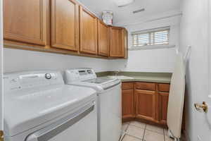 Laundry room featuring washing machine and clothes dryer, a sink, visible vents, cabinet space, and light tile patterned floors
