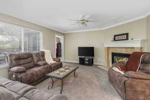 Carpeted living area with track lighting, baseboards, ceiling fan, crown molding, and a tile fireplace