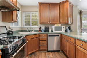Kitchen featuring light wood finished floors, under cabinet range hood, stainless steel appliances, a sink, and brown cabinetry