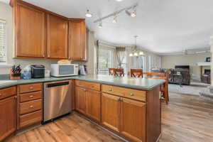 Kitchen with brown cabinets, dishwasher, white microwave, light wood-style flooring, and a peninsula