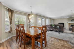 Dining area with a ceiling fan, a fireplace, ornamental molding, and light wood-type flooring