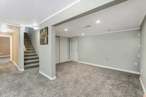 Finished below grade area featuring stairway, carpet, baseboards, ornamental molding, and visible vents