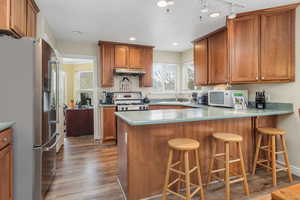 Kitchen with a sink, brown cabinets, light wood-style floors, appliances with stainless steel finishes, and under cabinet range hood