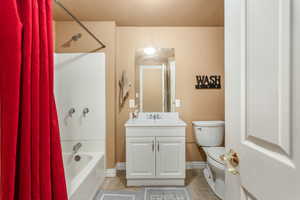 Full bathroom with tile patterned floors, toilet, vanity, shower / tub combo with curtain, and baseboards