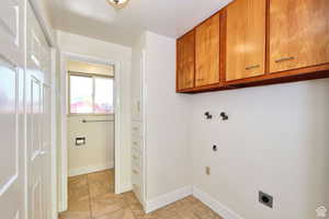 Washroom featuring electric dryer hookup, cabinet space, light tile patterned flooring, and baseboards