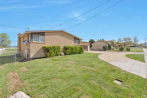 View of side of home with concrete driveway, a chimney, fence, a yard, and brick siding
