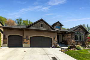 View of front of house featuring stucco siding, driveway, stone siding, a front yard, and a garage