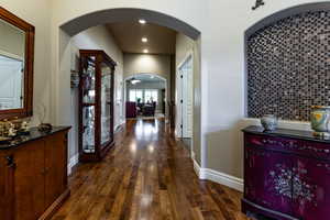 Hallway featuring recessed lighting, arched walkways, dark wood-style floors, and baseboards