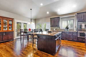 Kitchen with a breakfast bar, double oven, pendant lighting, dark wood-style floors, and a kitchen island