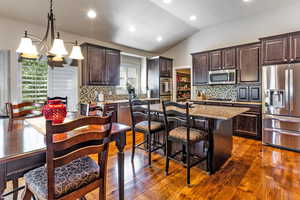 Kitchen featuring an island with sink, dark brown cabinetry, lofted ceiling, and appliances with stainless steel finishes