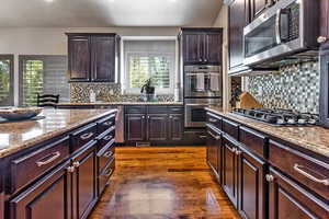 Kitchen with dark wood finished floors, backsplash, appliances with stainless steel finishes, and light stone counters