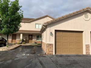 View of front of property featuring stucco siding, an attached garage, driveway, and stone siding