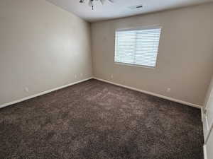 Unfurnished room featuring dark carpet, baseboards, a ceiling fan, and visible vents