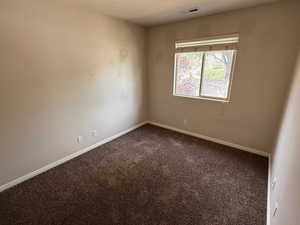 Empty room featuring baseboards, dark colored carpet, and visible vents