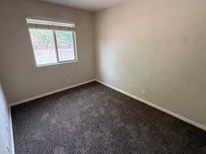 Empty room featuring baseboards and dark colored carpet