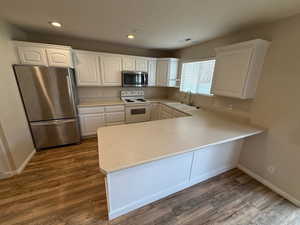 Kitchen featuring dark wood finished floors, a sink, a peninsula, appliances with stainless steel finishes, and white cabinetry