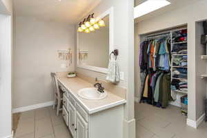 Bathroom with a walk in closet, baseboards, vanity, and tile patterned floors