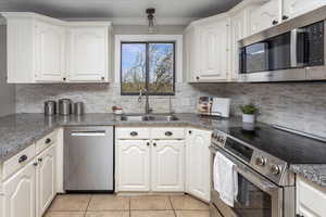 Kitchen with white cabinets, a sink, backsplash, appliances with stainless steel finishes, and ornamental molding
