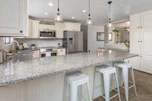 Kitchen with a sink, decorative light fixtures, a peninsula, appliances with stainless steel finishes, and light stone countertops