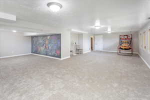 Finished basement featuring a textured ceiling, carpet flooring, and baseboards