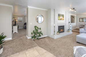 Carpeted living area with baseboards, a fireplace, a textured ceiling, and crown molding