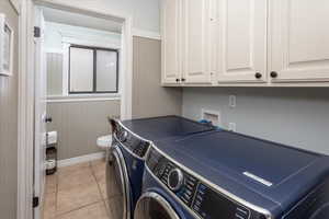 Laundry room featuring wood walls, laundry area, light tile patterned flooring, washing machine and clothes dryer, and baseboards