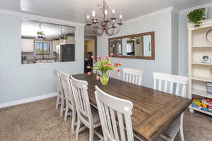 Dining space featuring light carpet, crown molding, baseboards, a textured ceiling, and a notable chandelier