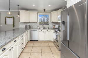Kitchen with a sink, decorative backsplash, light tile patterned flooring, appliances with stainless steel finishes, and ornamental molding