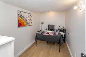 Home office featuring light wood-style floors, a textured ceiling, and baseboards