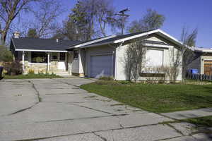 Ranch-style home featuring a garage, driveway, a chimney, and a front lawn