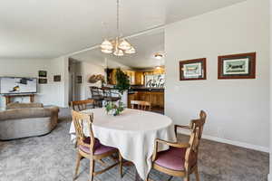 Carpeted dining room with vaulted ceiling, baseboards, and an inviting chandelier