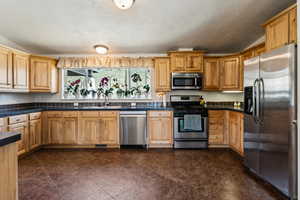 Kitchen featuring stainless steel appliances, a sink, a textured ceiling, and dark countertops