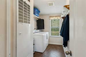 Laundry area with washer and clothes dryer, a heating unit, baseboards, dark tile patterned flooring, and laundry area