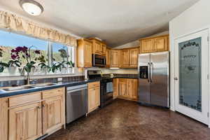 Kitchen featuring a sink, a textured ceiling, dark countertops, lofted ceiling, and appliances with stainless steel finishes