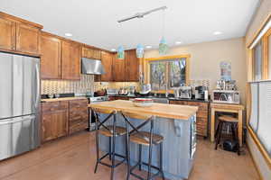 Kitchen with a sink, decorative backsplash, butcher block counters, stainless steel appliances, and under cabinet range hood