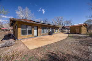 Back of property with roof mounted solar panels, an outbuilding, a shed, and a patio