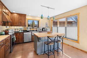 Kitchen with recessed lighting, under cabinet range hood, decorative backsplash, a kitchen bar, and appliances with stainless steel finishes