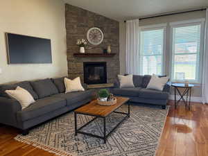 Living room with vaulted ceiling, wood finished floors, and a stone fireplace