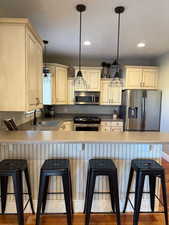 Kitchen featuring a sink, a breakfast bar area, cream cabinets, stainless steel appliances, and a peninsula