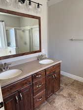 Full bath with baseboards, a sink, double vanity, and a stall shower