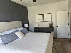 Bedroom with baseboards, a ceiling fan, dark colored carpet, and a decorative wall