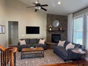 Living room with vaulted ceiling, a stone fireplace, a ceiling fan, wood finished floors, and baseboards