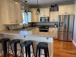 Kitchen featuring stainless steel appliances, a peninsula, a sink, light wood-style floors, and a kitchen bar