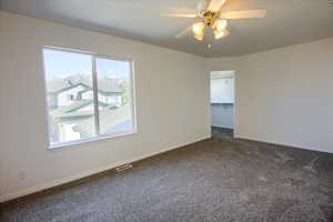 Empty room featuring baseboards, visible vents, dark carpet, and ceiling fan