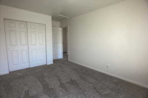 Unfurnished bedroom with attic access, baseboards, dark carpet, and a closet