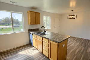 Kitchen with a peninsula, stainless steel dishwasher, a sink, visible vents, and wood finished floors