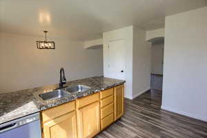 Kitchen with stainless steel dishwasher, a sink, light brown cabinetry, arched walkways, and dark wood-style flooring